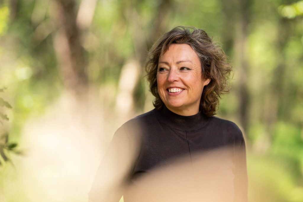 Smiling woman outside in wooded area.