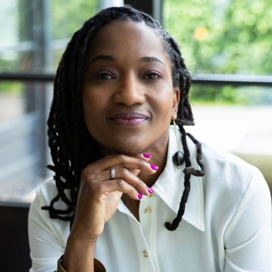 Vrouw in witte blouse glimlacht bij raam.